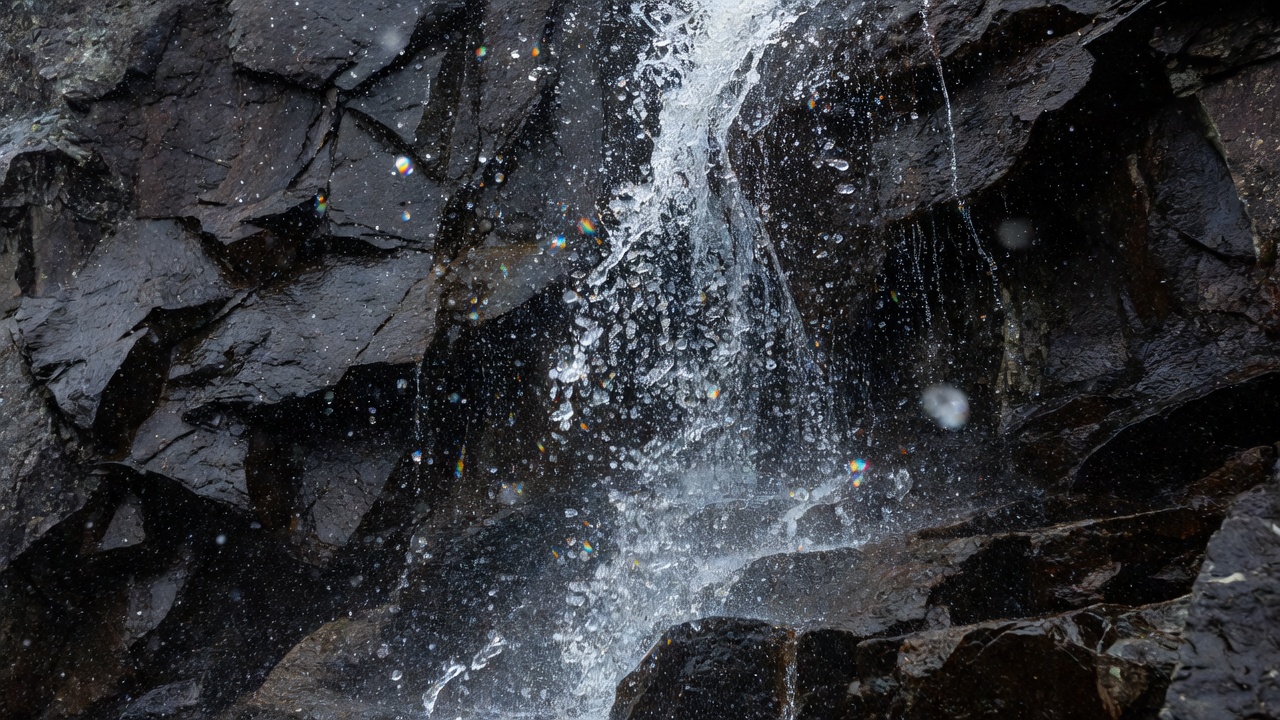 Bright droplets of waterfall spray suspended in front of dark fractured rock